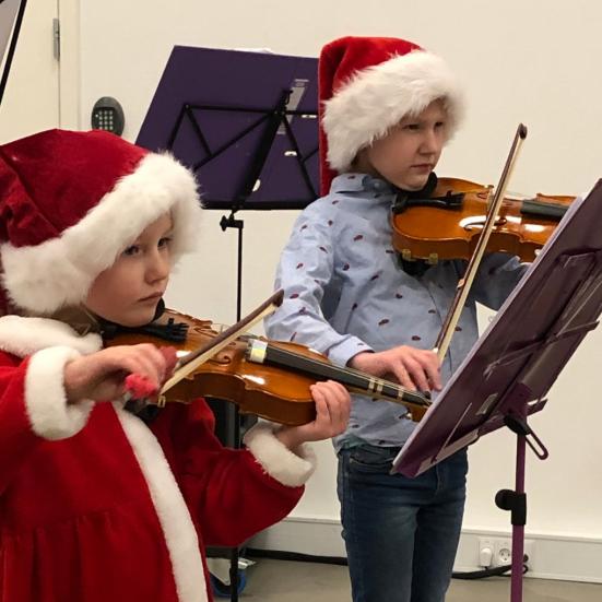 To børn spiller violin med nissehuer på.
